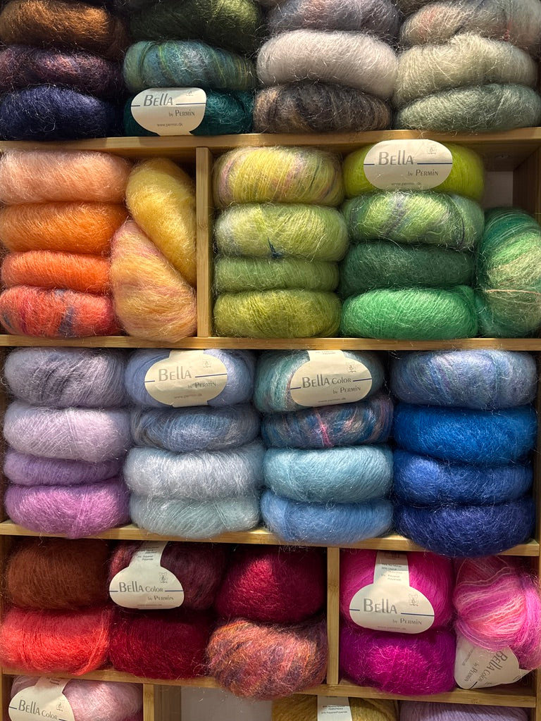 Shelves filled with colorful yarn skeins labeled 'Bella' in a store setting.