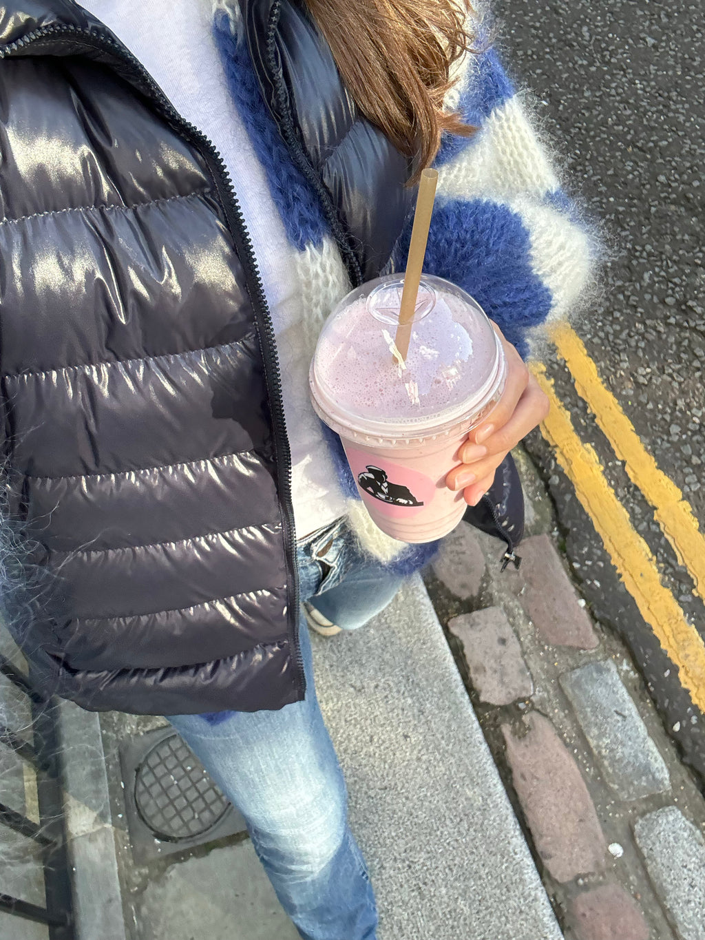 Person holding a pink iced coffee on a sidewalk