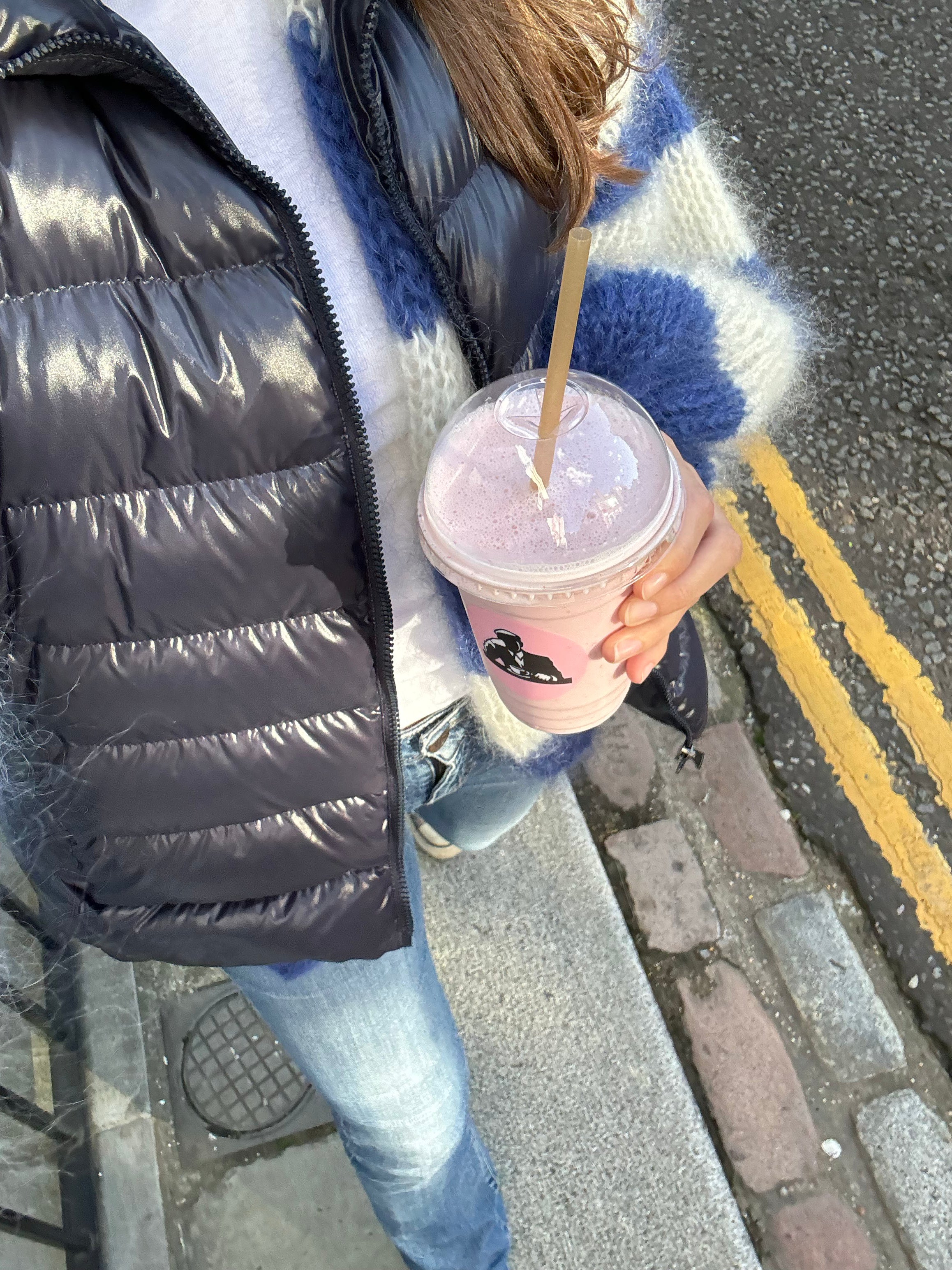 Person holding a pink iced coffee on a sidewalk