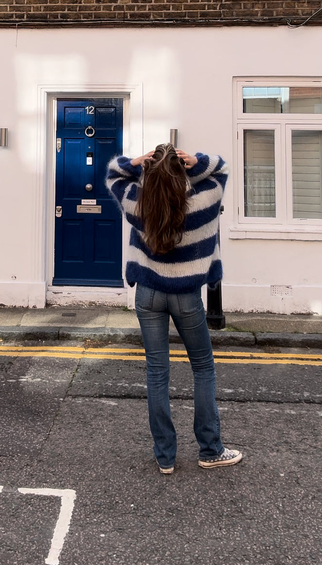 Person wearing a blue and white striped sweater standing on a street with a blue door and window in the background.
